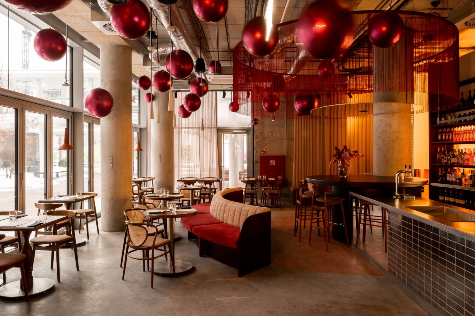 Sala restauracji w dziennym świetle: betonowe słupy, czerwone kule pod sufitem